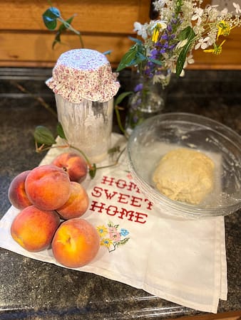 Peaches and sourdough starter and dough on the counter with flowers in the background