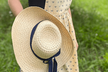 girl in a field wearing an apron holding a straw hat