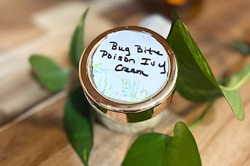 small jar with the label bug bite poison ivy cream with plant leaves all around it