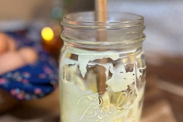 Mayo in a mason jar with a wooden spatula. A basket of eggs and a lit candle in the background