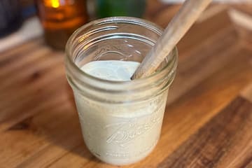 ranch dressing in a jar with a wooden spatula with a candle and a plant in the background