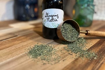 bottle on a wooden counter with loose herbs spilling out of a measuring cup