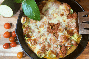cast iron skillet on a wooden counter with rolled up zucchini slices and tomato sauce and cheese