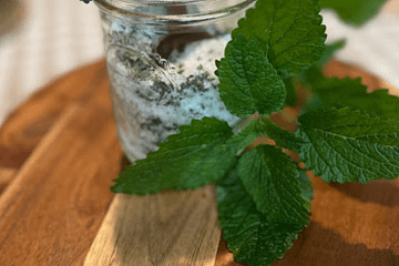 jar of bath salt on a wooden stand with a lavender sprig and a lemon balm sprig next to it