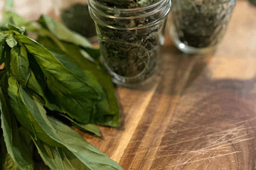 several jars of dried herbs on a cutting board with fresh herbs to the side of it