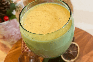 Glass of eggnog on a wooden stand with cinnamon sticks and orange slices on the stand