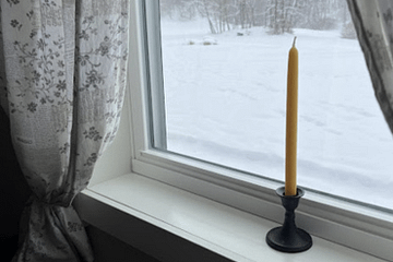 a candle in a window looking out on a winter landscape