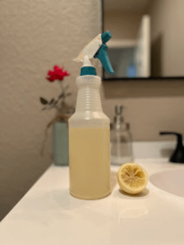 Bottle of liquid on a bathroom sink with a half of a lemon on the counter next to it