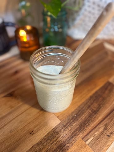 Ranch dressing in a mason jar with a wooden spatula and a candle and plant in the background