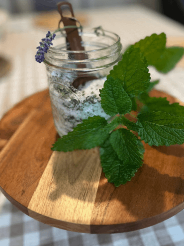 jar of salt and dried herbs on a wooden stand with a lavender sprig and a lemon balm leaf