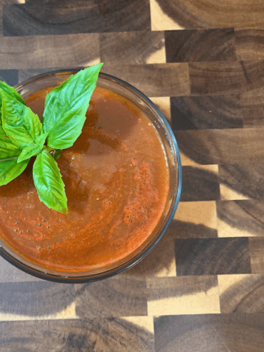 Spaghetti sauce in a bowl with a basil leaf on a wooden cutting board